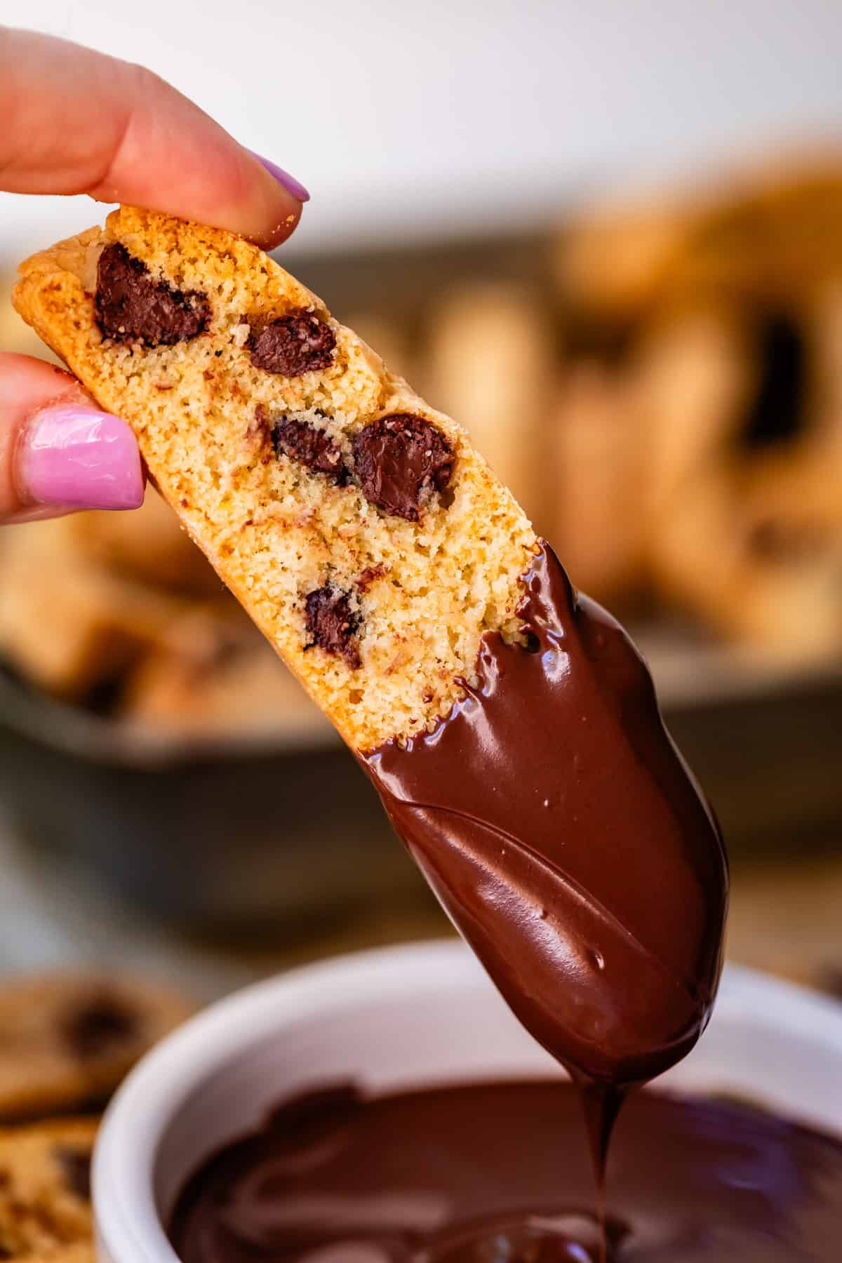 finger and thumb dipping a baked biscotti cookie into chocolate.