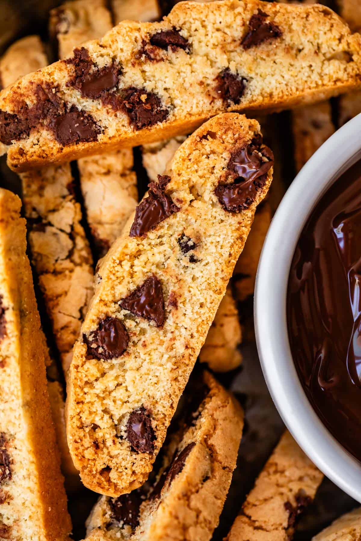 several chocolate chip biscotti cookies next to a bowl of melted chocolate.