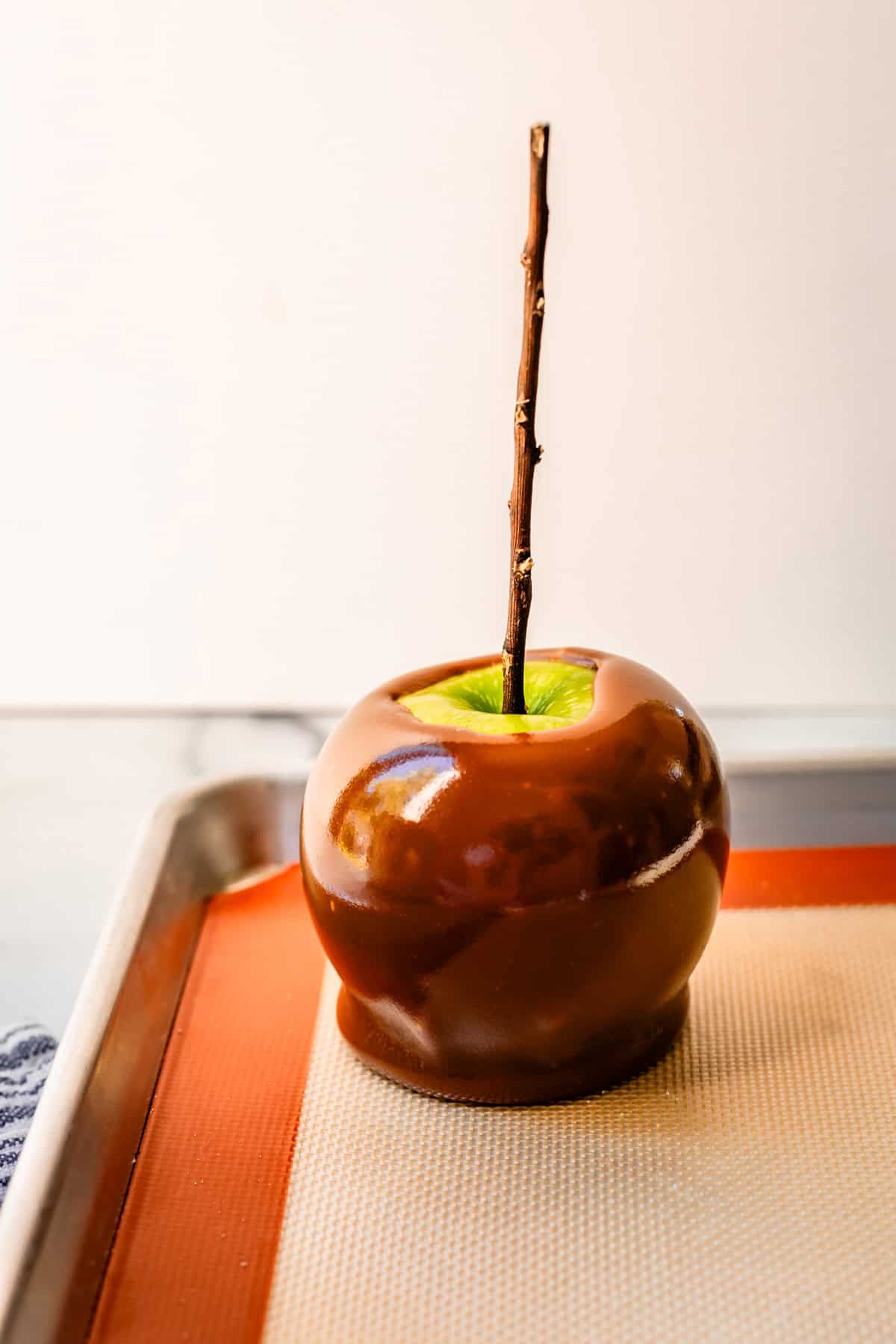a completely dipped caramel apple with a stick in it resting to cool on a silpat.