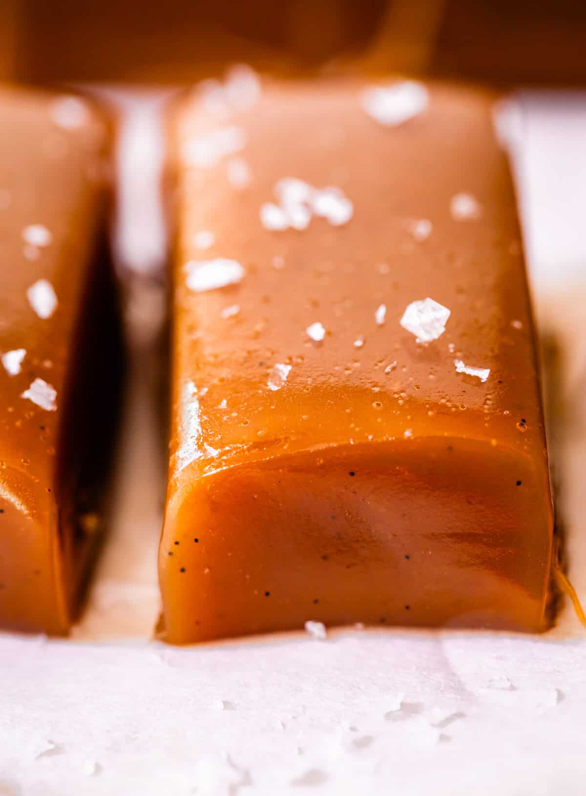 sideways view of one rectangle piece of vanilla specked soft caramel with flaky salt garnish.
