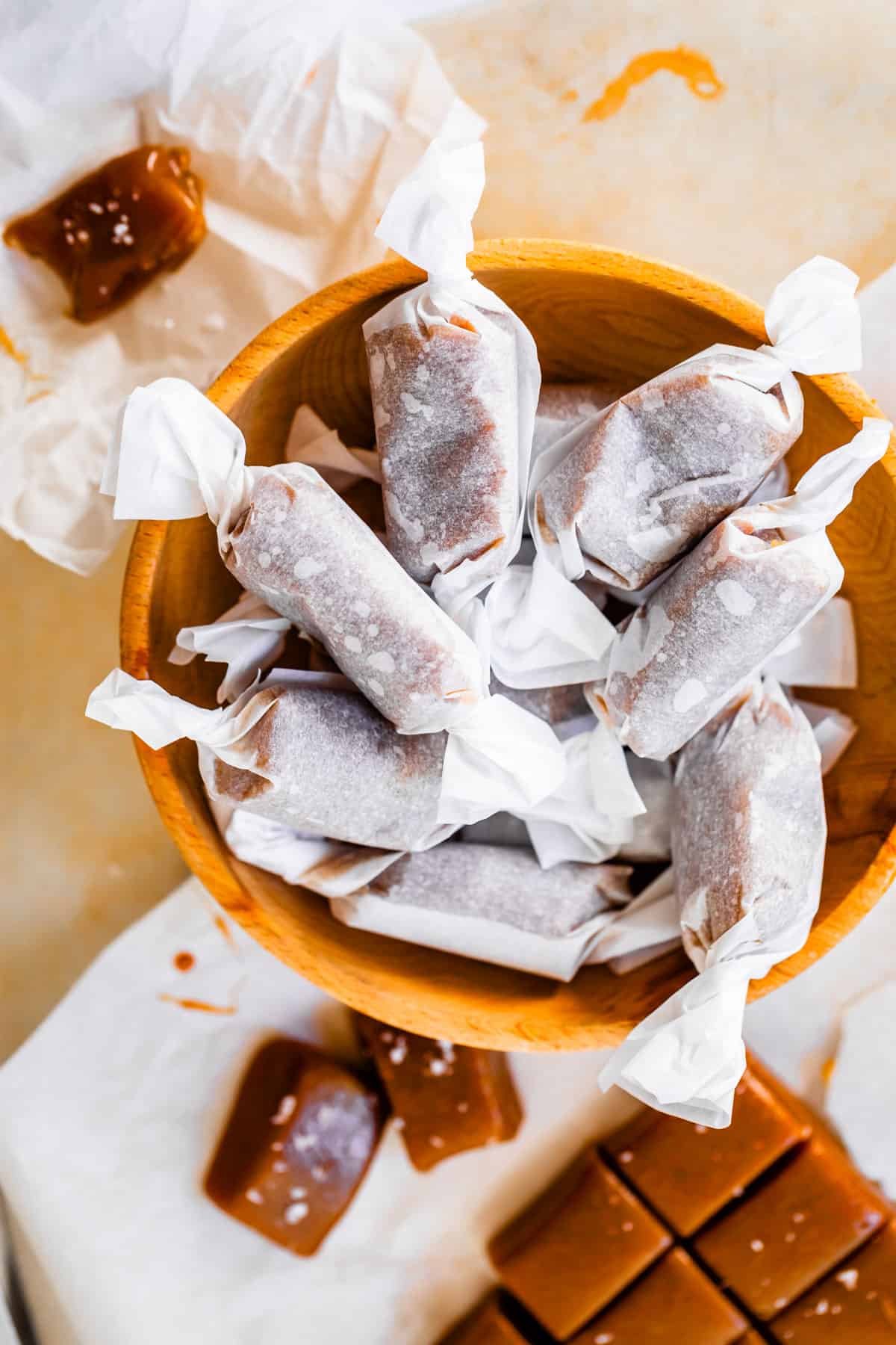 a wooden bowl filled with wax wrapped soft caramel candies.