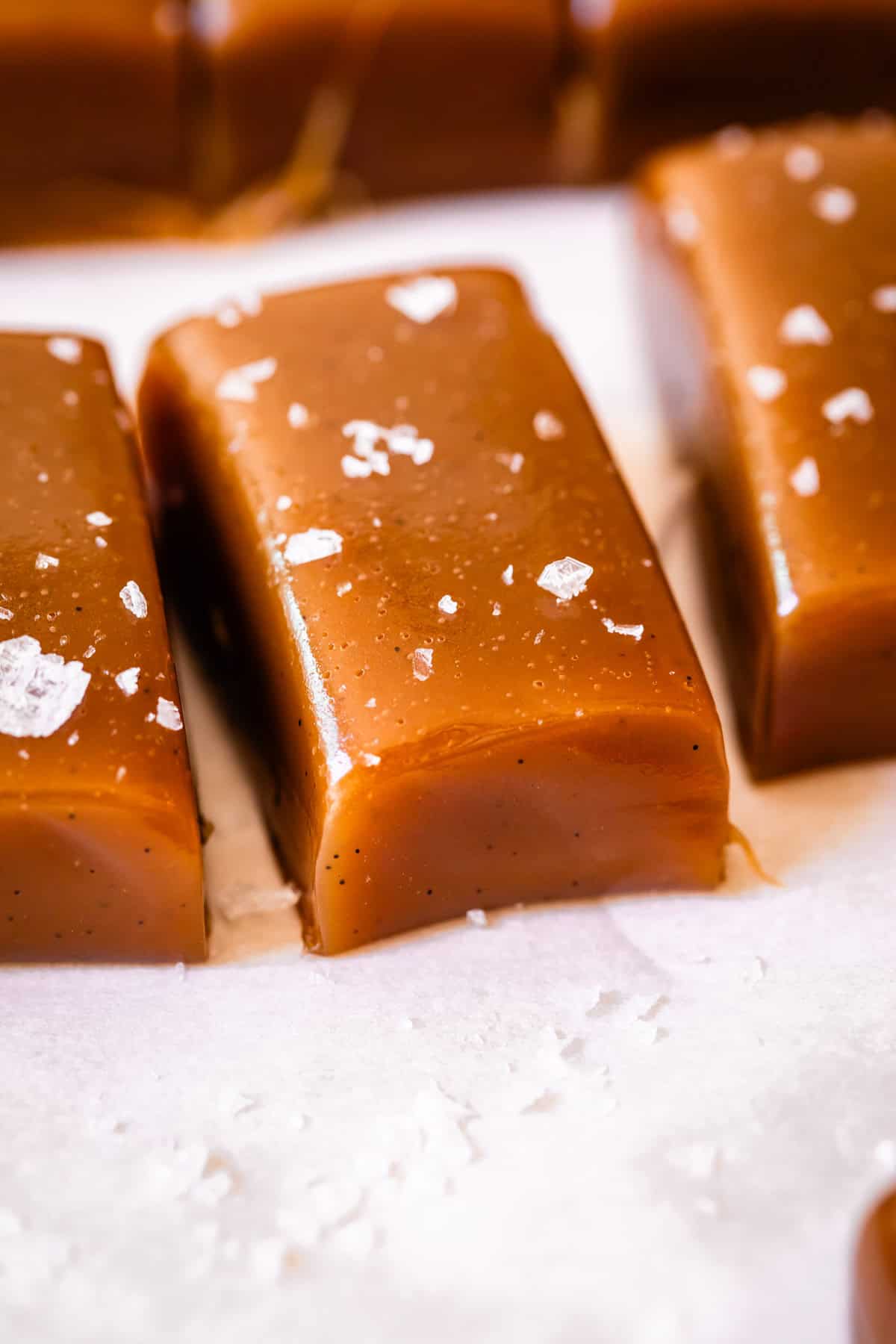 a cut rectangle caramel candy piece topped with flaky salt on parchment paper.