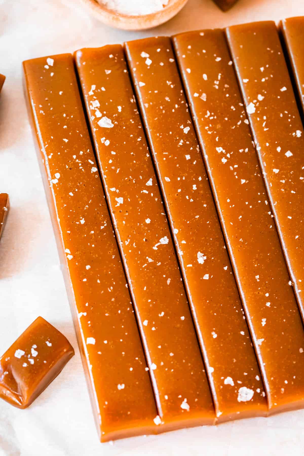 square of soft caramel candy topped with flaky salt, sliced into 6 long columns.