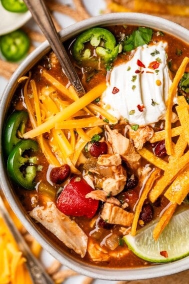 bowl with chicken tortilla soup topped with cheese, sour cream, fried tortilla strips, and more.