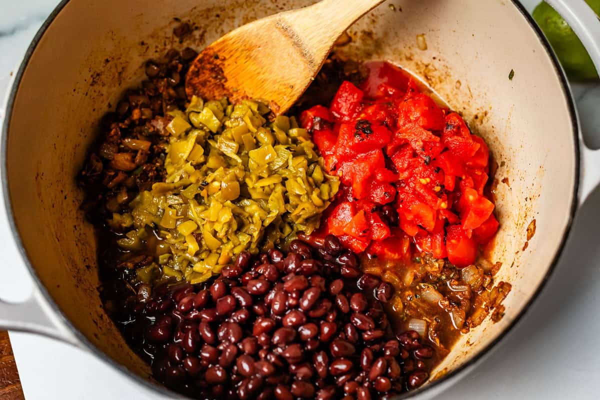 fire roasted tomatoes, green chilies, and black beans in a pot with the onions and spices.