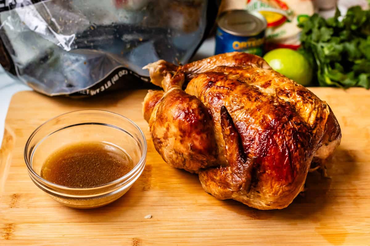 rotisserie chicken on a cutting board with a bowl of drippings on the side.