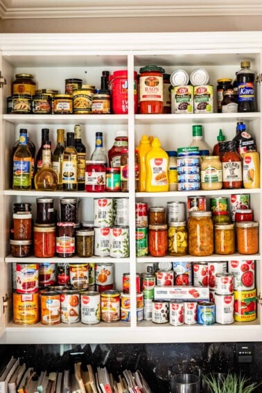 picture of white cupboards open to show pantry items like mustard, canned goods, pasta sauce, vinegar, etc.