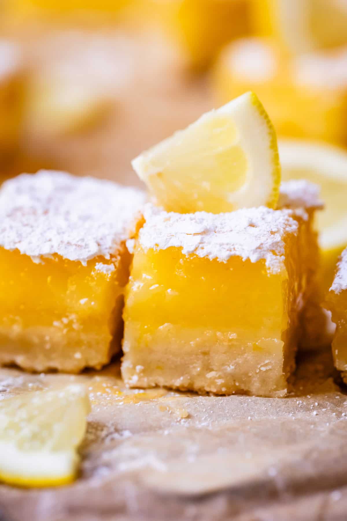 close up of a lemon bar with thick custard filling and a small lemon wedge garnish.