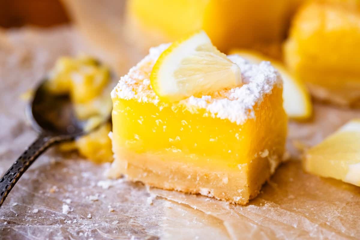 close up of a perfectly cut lemon square, topped with powdered sugar and lemon.