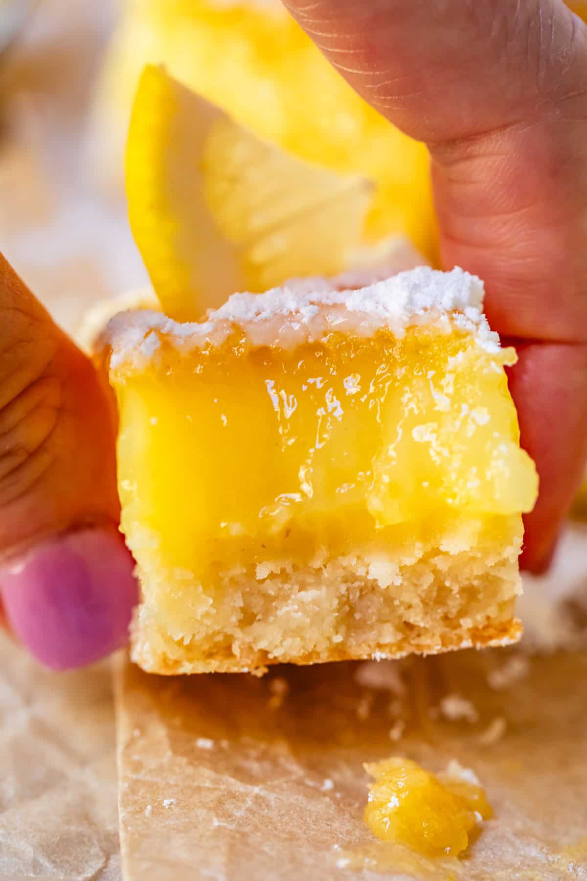 thumb and finger holding a lemon square with a bite taken from it.
