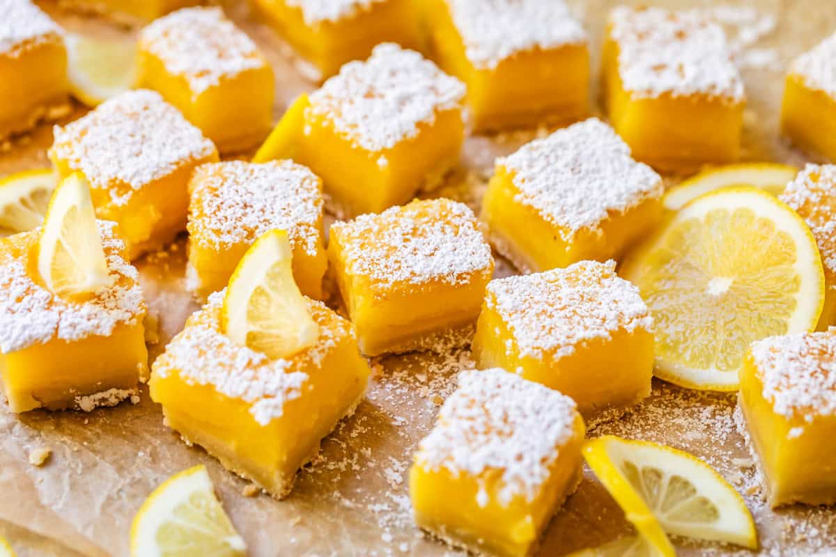 lemon squares with powdered sugar and lemon garnish on parchment paper.
