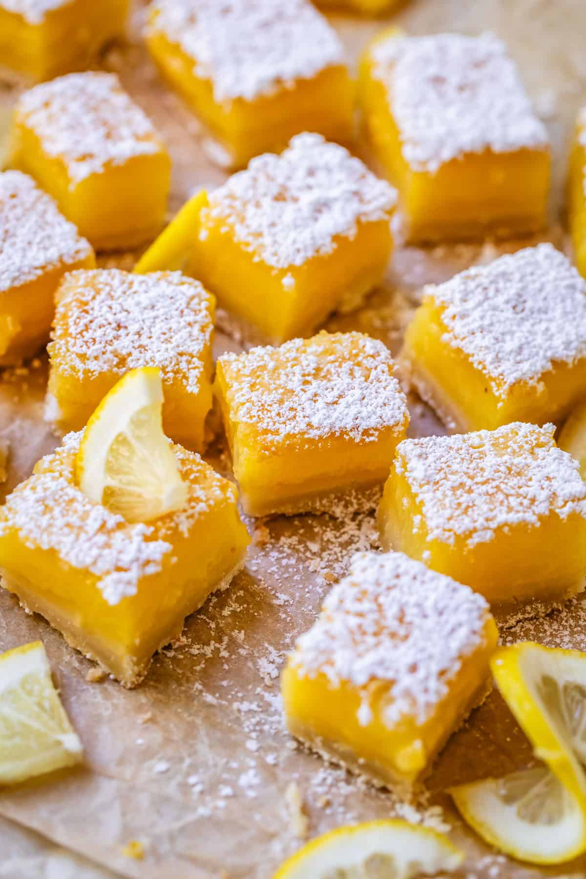 several lemon bar squares dusted with powdered sugar on parchment paper.