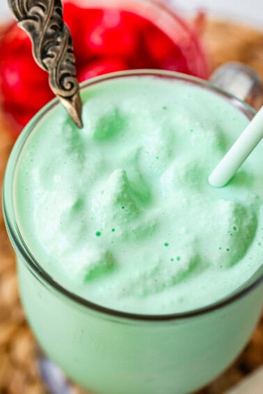glass mug with shamrock shake with a spoon and a straw in it.
