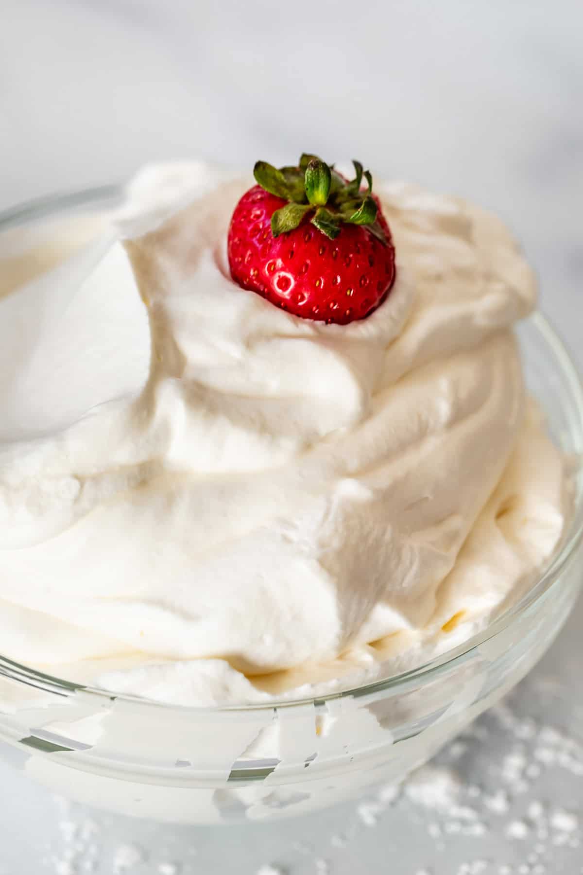 glass bowl filled over the top with pillowy whipped cream, with a strawberry in the top.