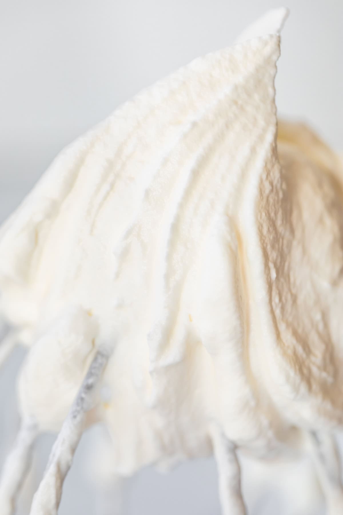 close up of stiff peak of whipped cream on a kitchen aid whisk attachment.