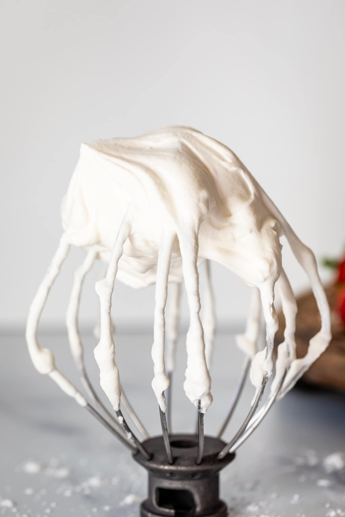 whipped cream on a stand mixer whisk attachment on a marble counter.