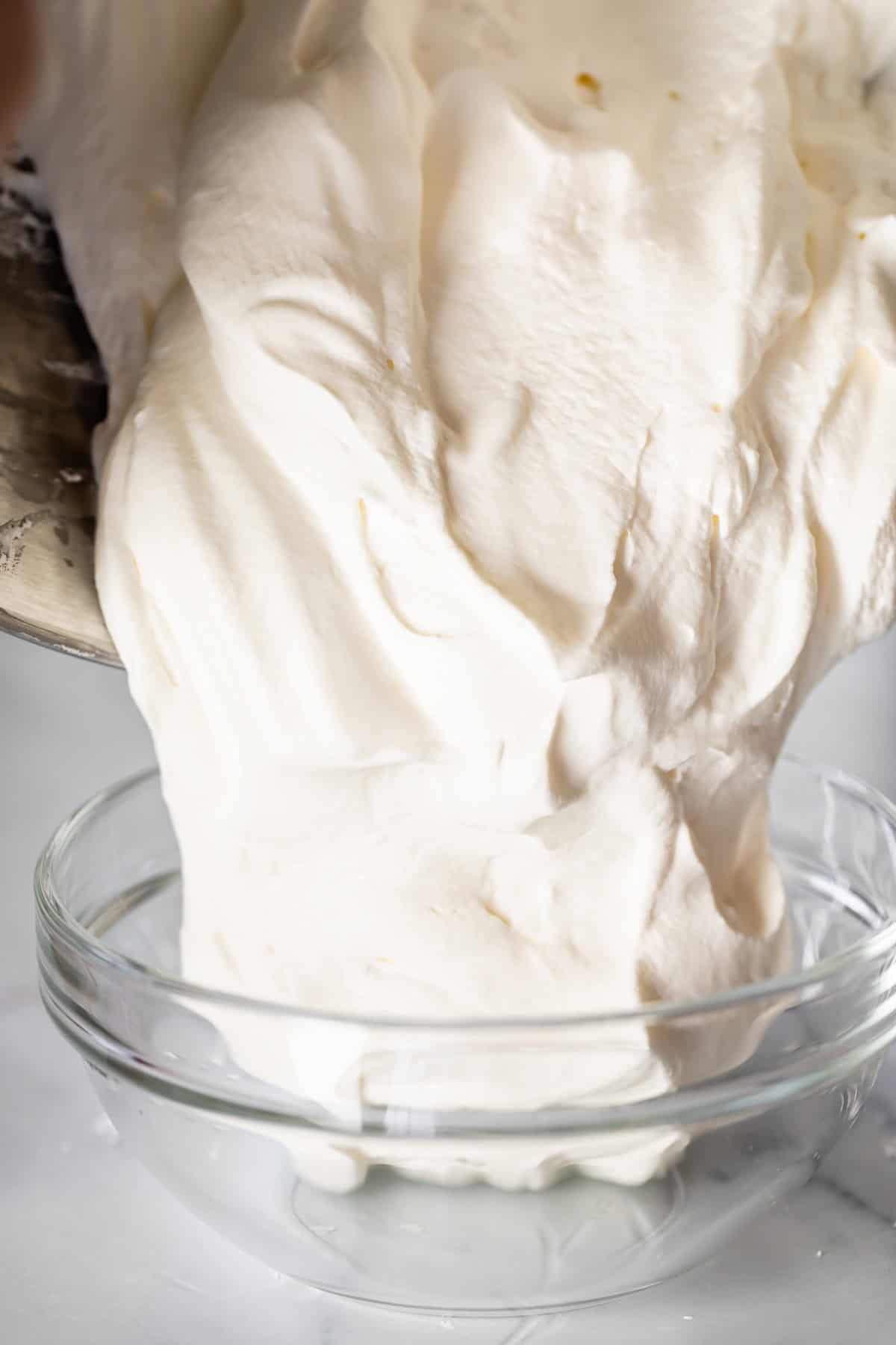 pouring whipped cream from a metal mixer bowl into a glass bowl.