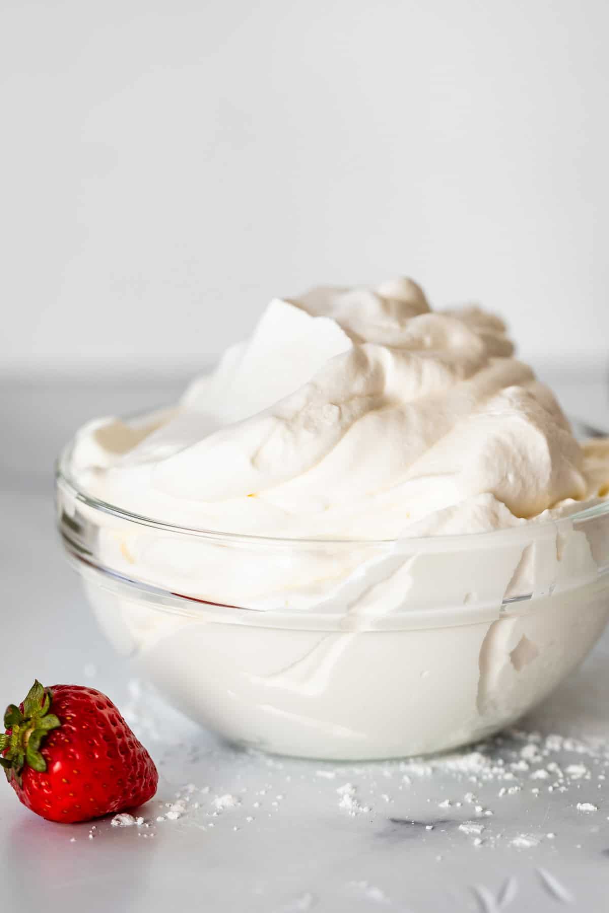 glass bowl with whipped cream and single strawberry on marble counter .