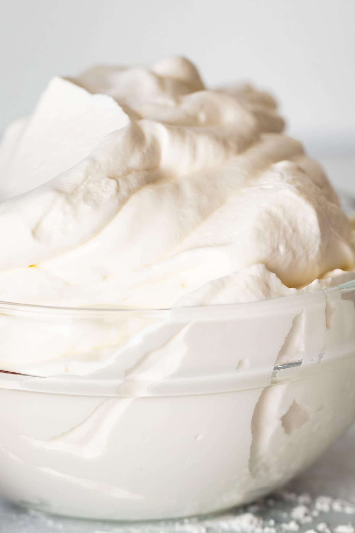 close up of glass bowl sitting on marble counter, piled high with whipped cream.