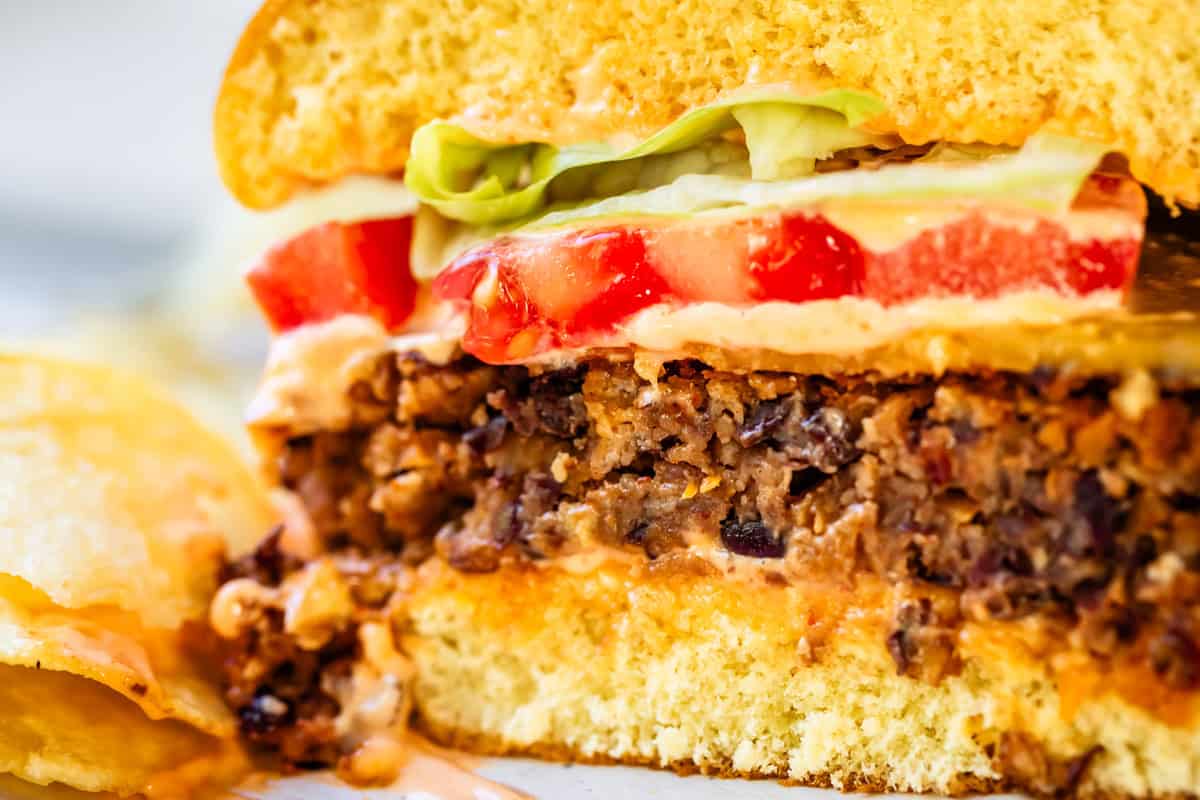 cross section of a black bean burger on a bun with veggies and cheese, chips on the side.