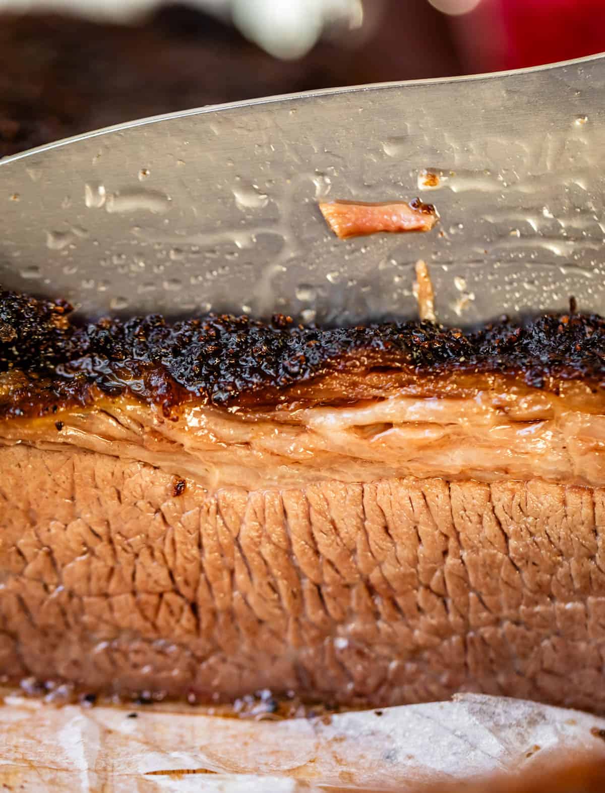 knife cutting into brisket to show the smoked bark on top and the cross cut of the grain.