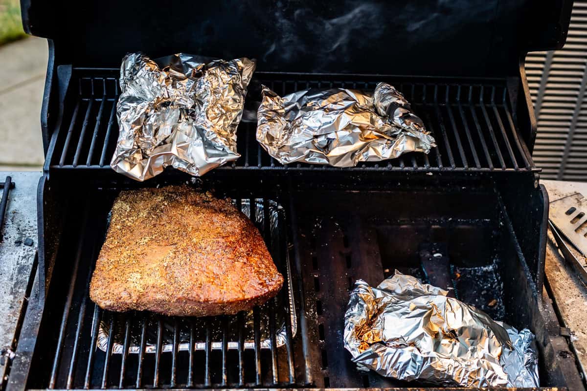 3 foil packets in a grill with a brisket.