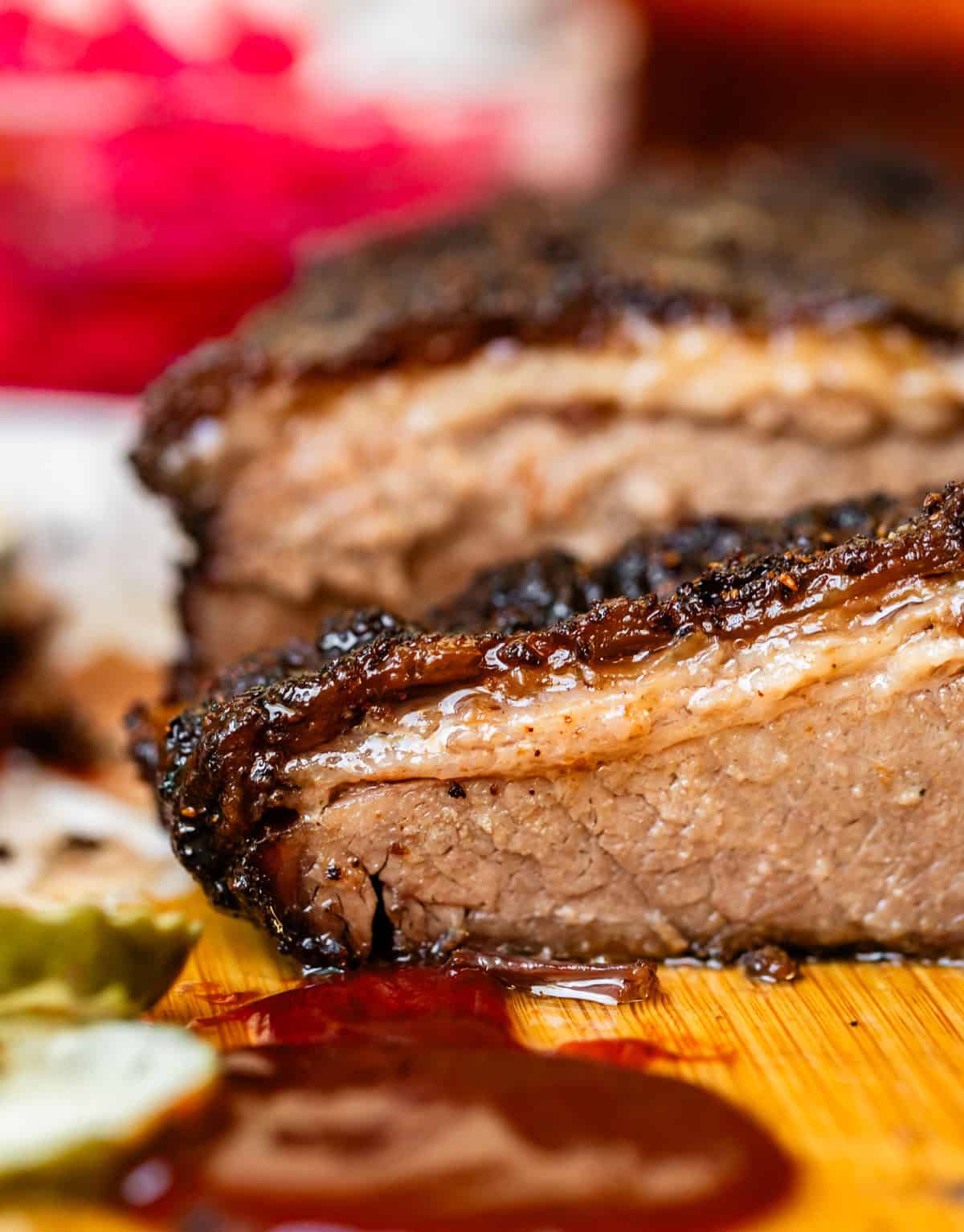 Crosscut section of beef brisket on cutting board with pickles.