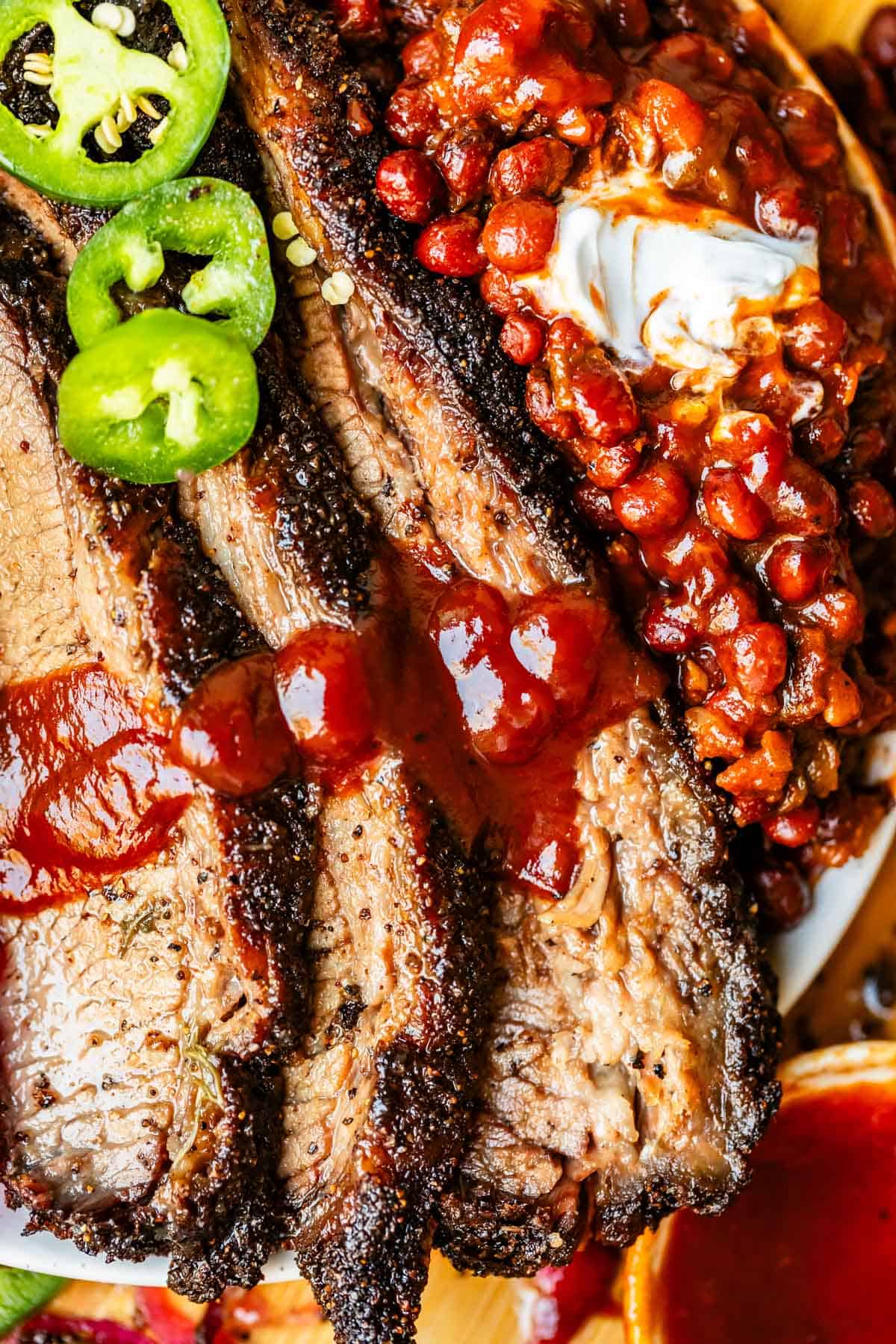 Overhead shot of beef brisket with barbecue sauce, beans, and jalapeño on a white plate.