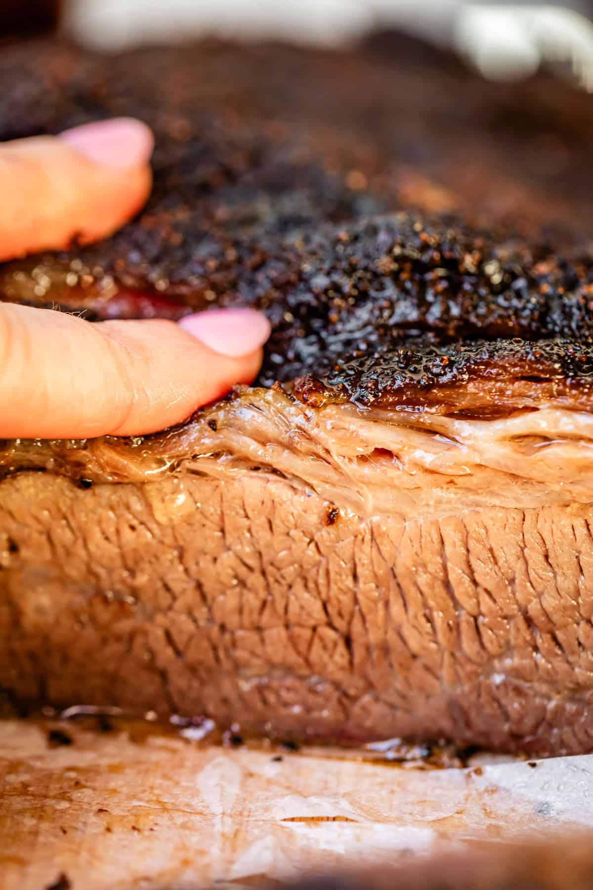 Juicy beef brisket crut showing charred top edge close up with fingers.
