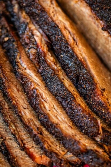 Laid out slices of beef brisket with seared fat-cap close up.