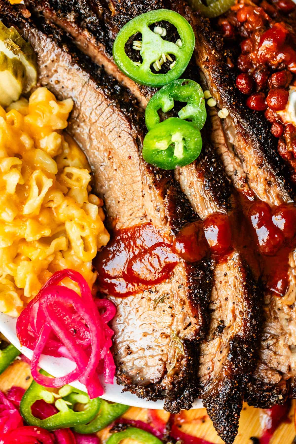Plate of slices of beef brisket with mac & cheese and beans with bbq sauce.