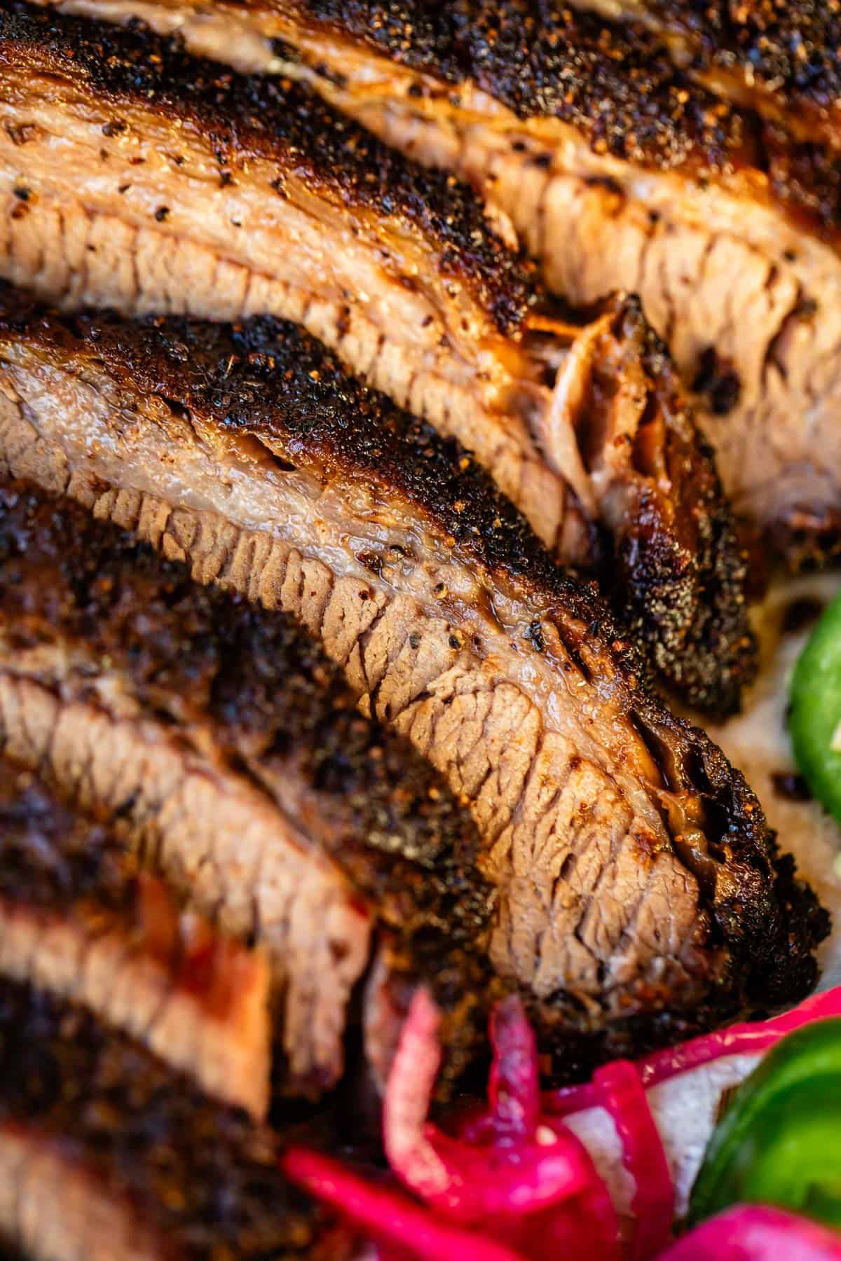 Slices of beautifully charred beef brisket laid out with jalapeño and pickled onions.