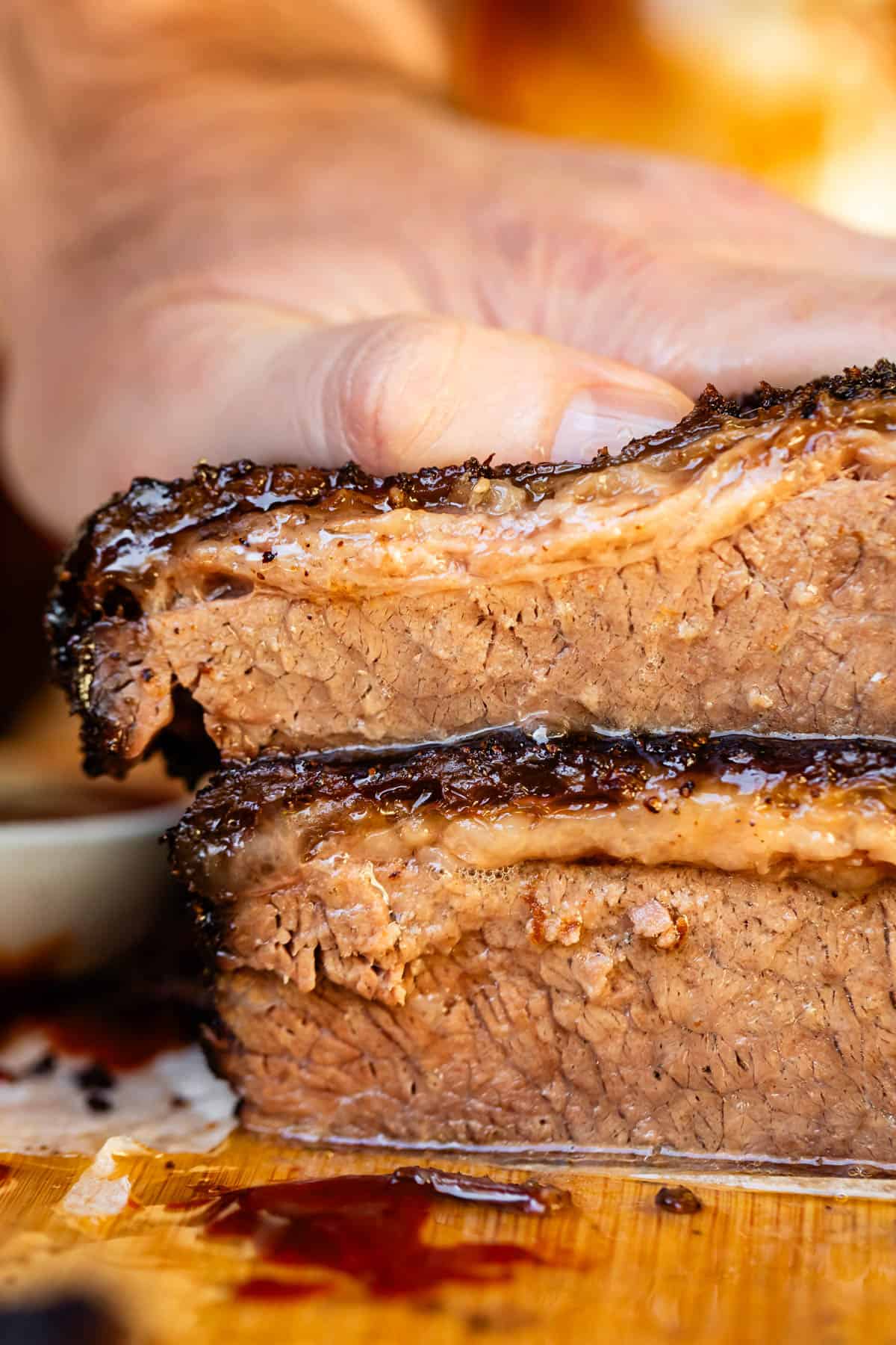 Juicy brisket cross cut stacked on wooden cutting board.