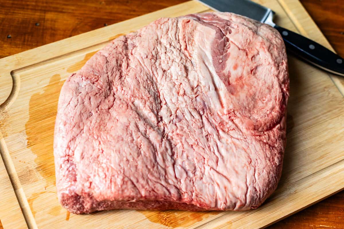brisket flat sitting on a wooden cutting board with a knife next to it.