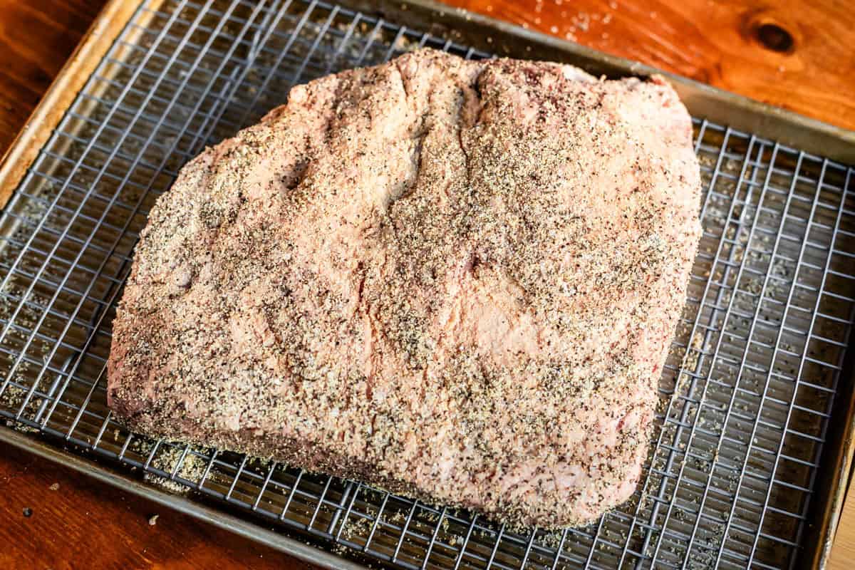 brisket covered in dry brine of salt, pepper, and garlic sitting on a tray on a sheetpan.
