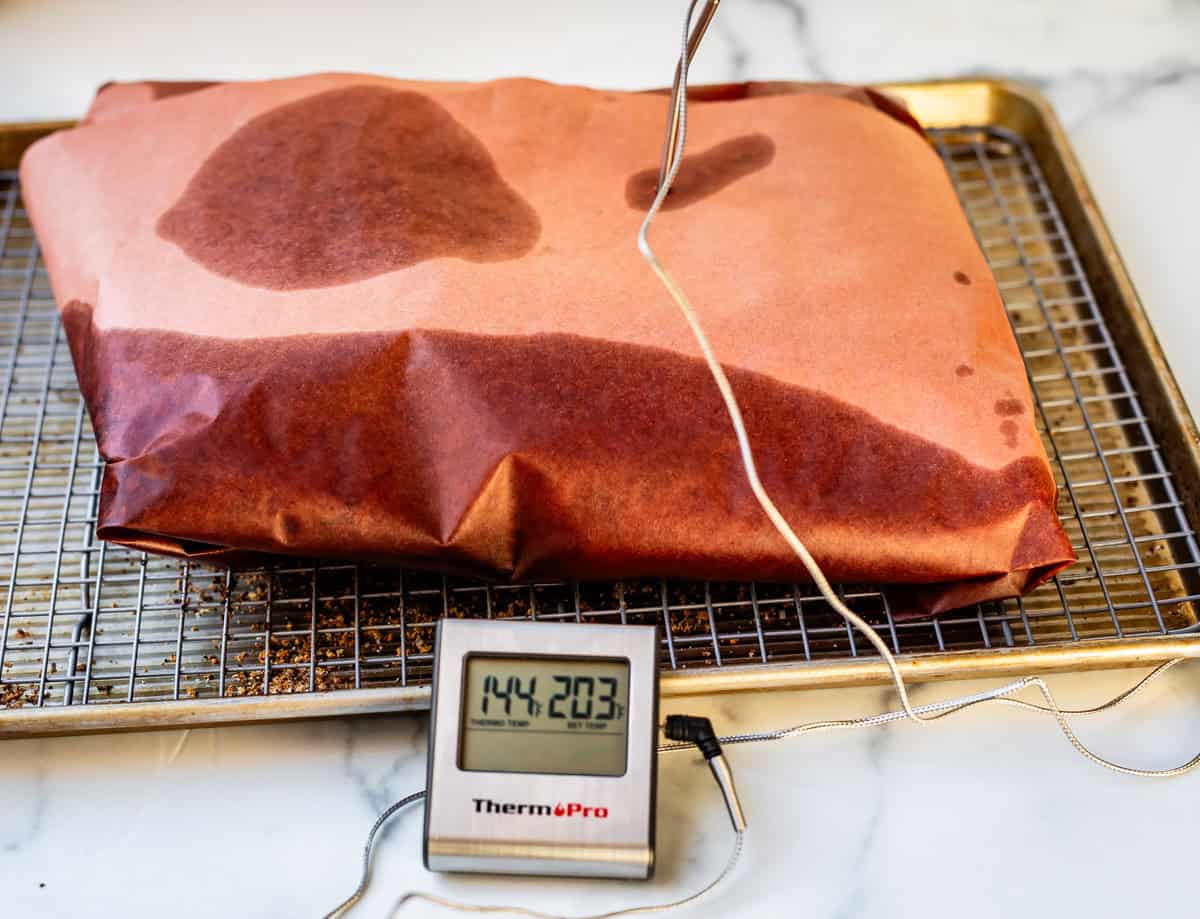 butcher paper wrapped brisket on baking sheet with thermometer reading 203 degrees.
