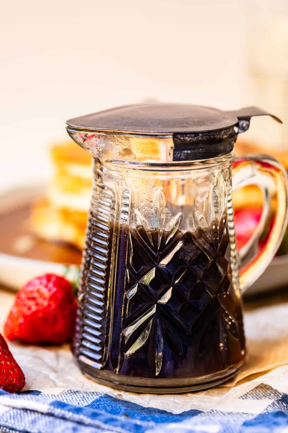 a pitcher of syrup next to fresh fruit.
