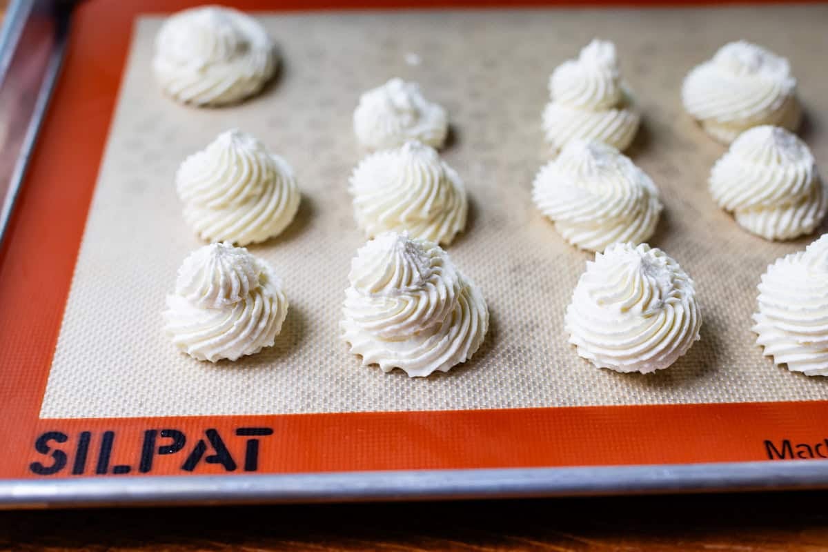 whipped cream piped into individual swirls on a silpat on a baking sheet.