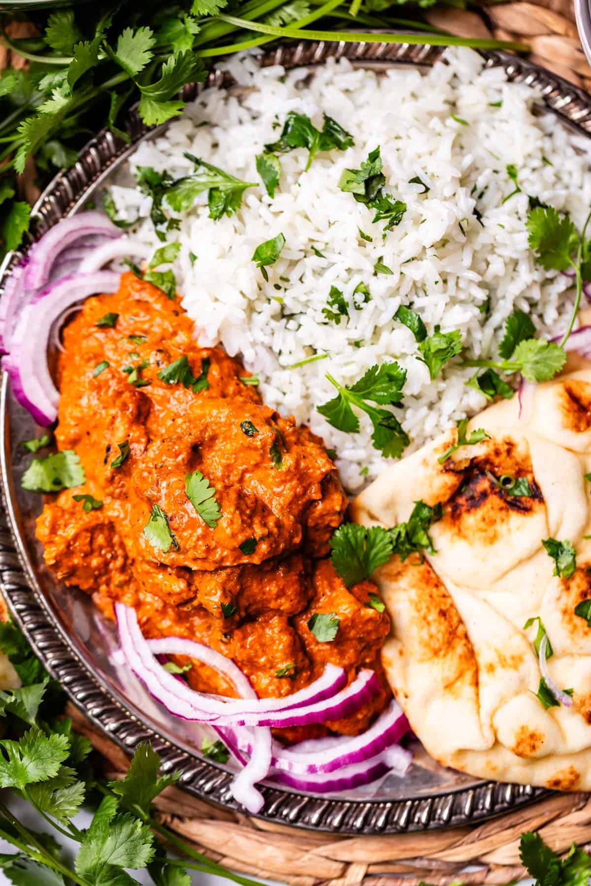 looking down on a metal tray with a serving of rice, naan, and tikka masala with red onion garnish.