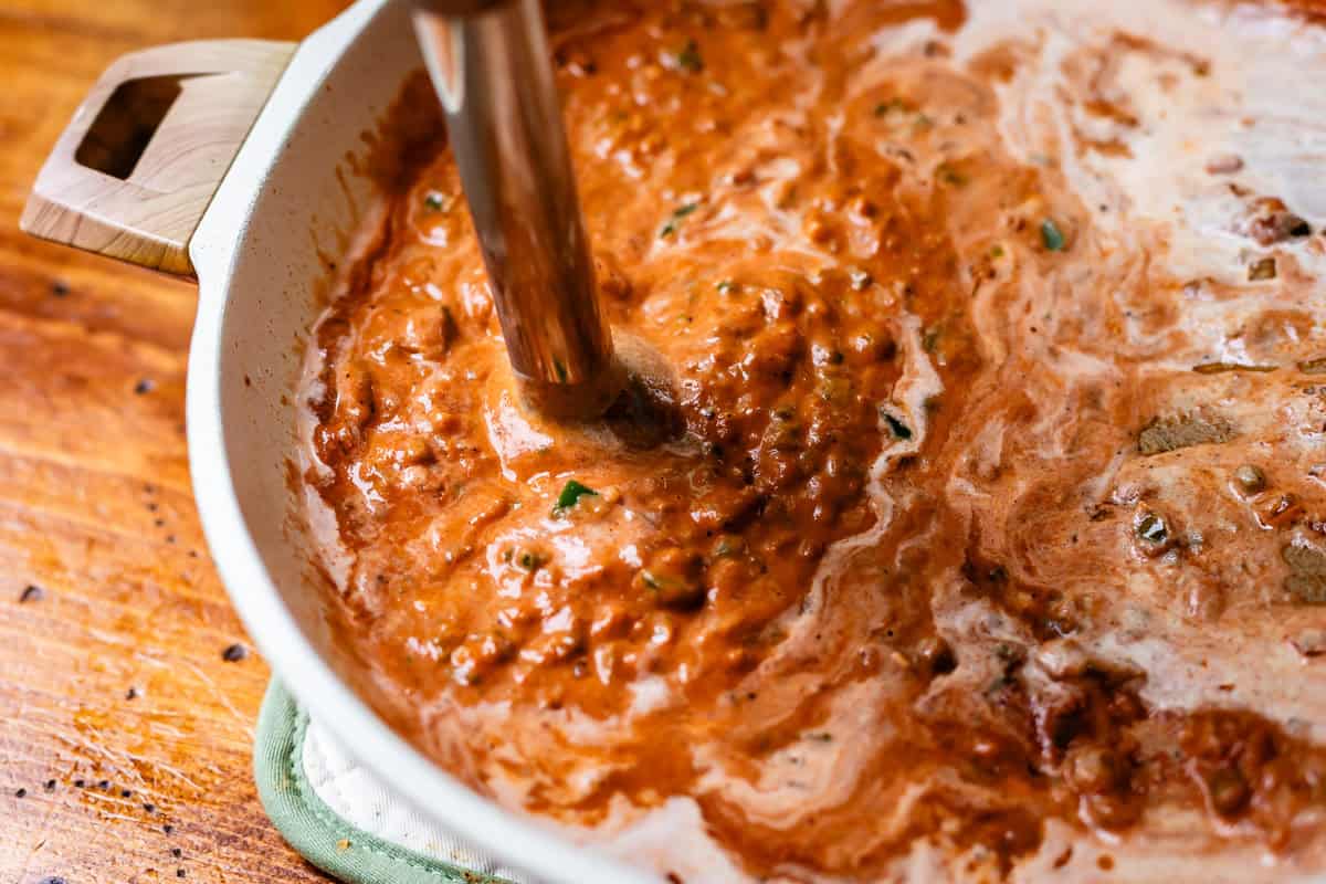 an immersion blender stuck into the pan with unblended sauce.