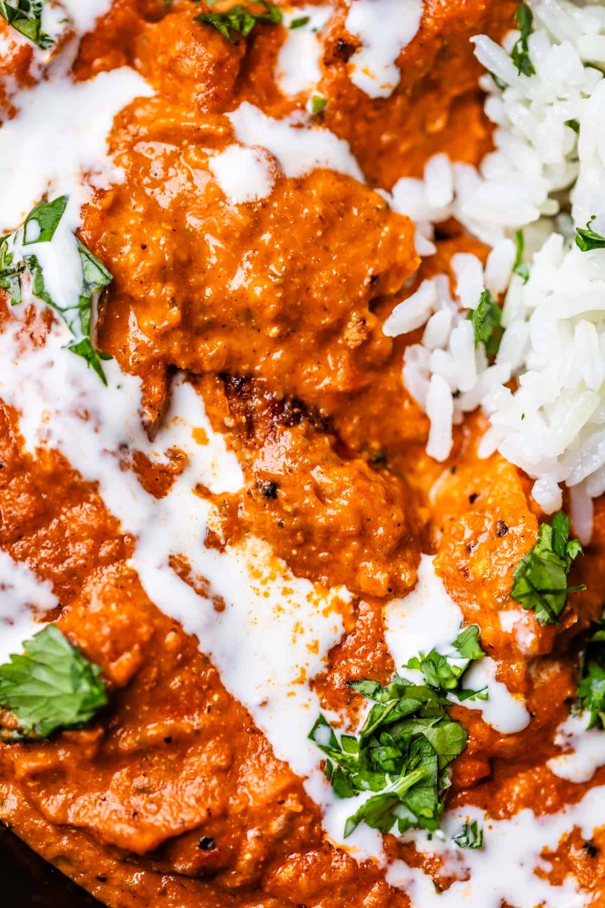close up of chicken tikka masala with cream and parsley garnish and rice.