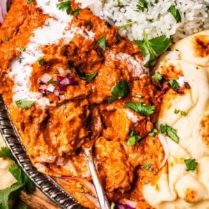 looking down on a metal tray with a serving of rice, naan, and tikka masala with a spoon.