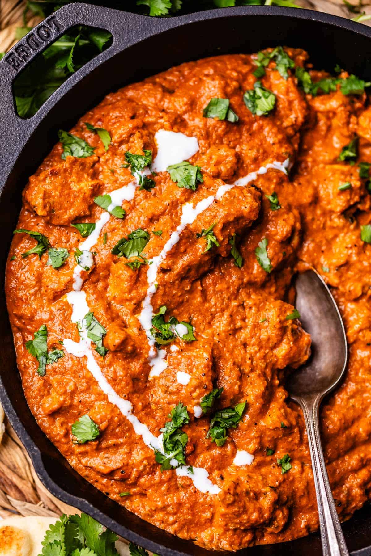 cast iron skillet filled with tikka masala, garnished with cream and parsley, with a spoon in it.