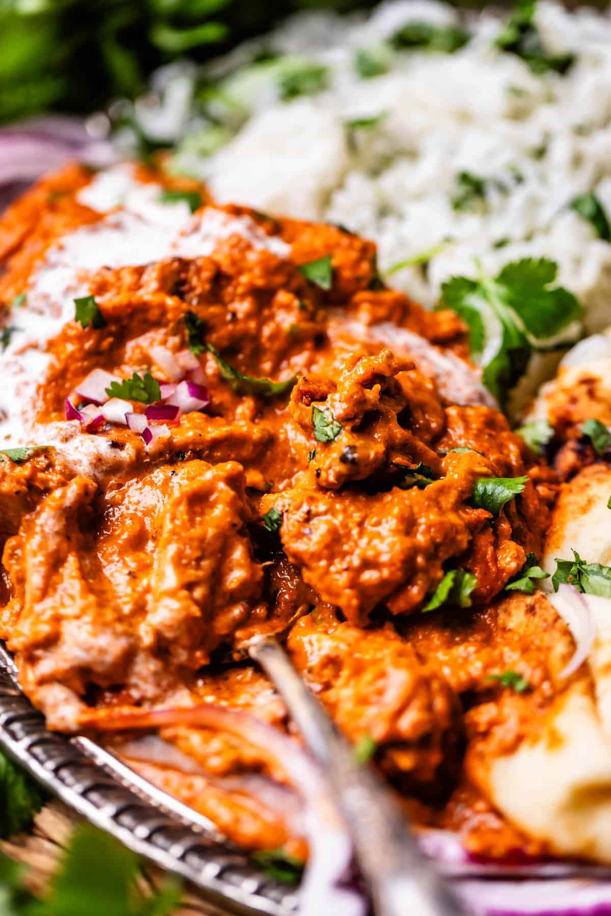 side view of a metal tray of chicken tikka masala with rice and naan sides.