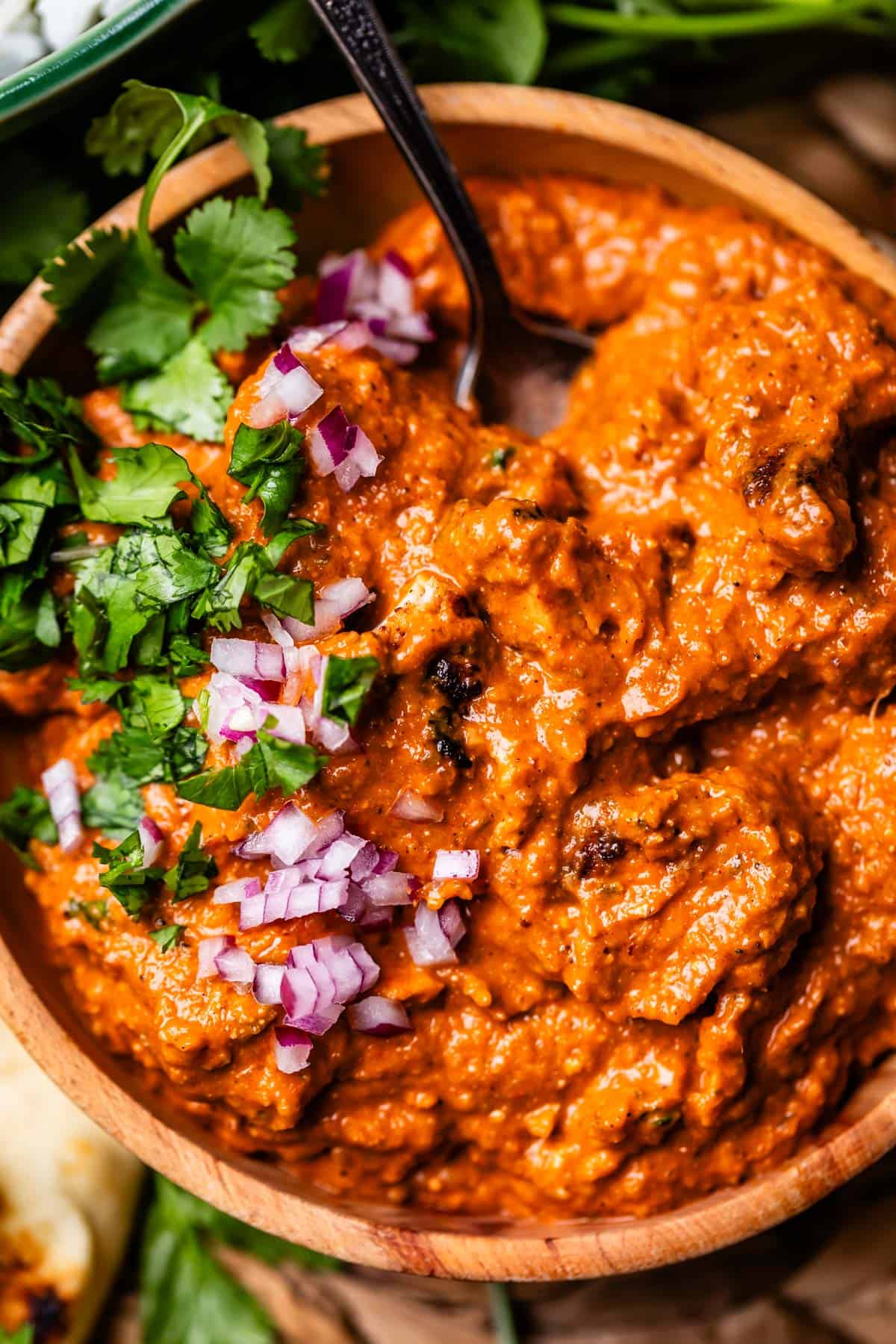 wooden bowl filled with chicken tikka masala with red onion and cilantro garnish.