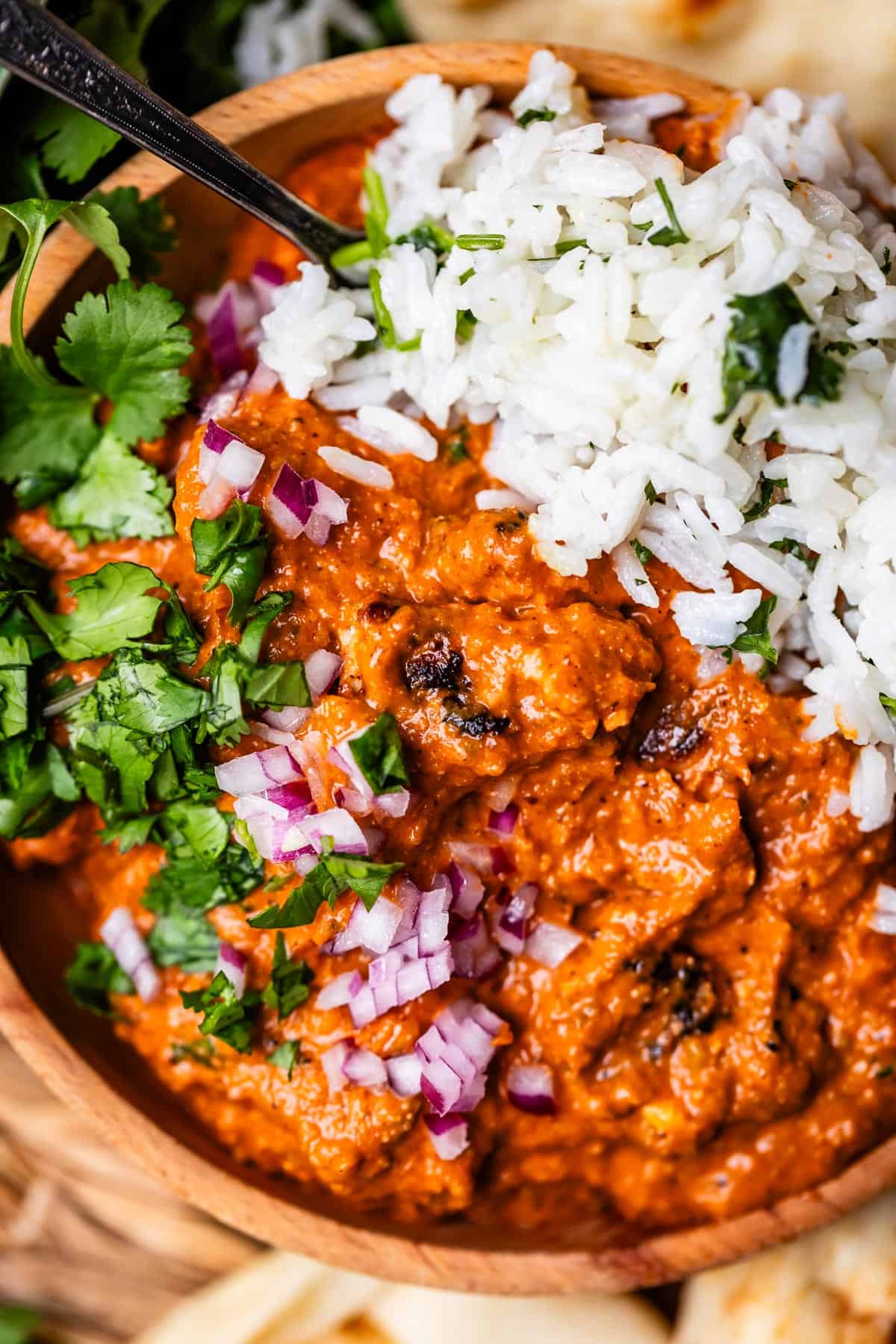 wooden bowl filled with chicken tikka masala and rice with red onion and cilantro garnish.