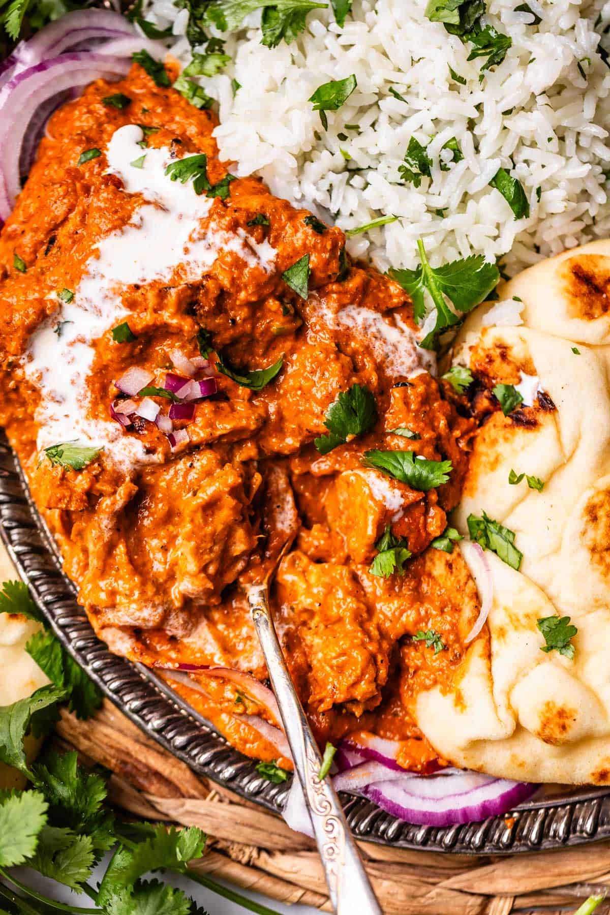 looking down on a metal tray with a serving of rice, naan, and tikka masala with a spoon.