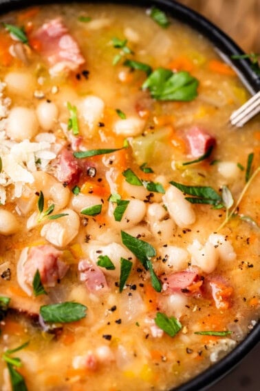 close up looking at ham and bean soup with garnish like cheese, parsley, and pepper.