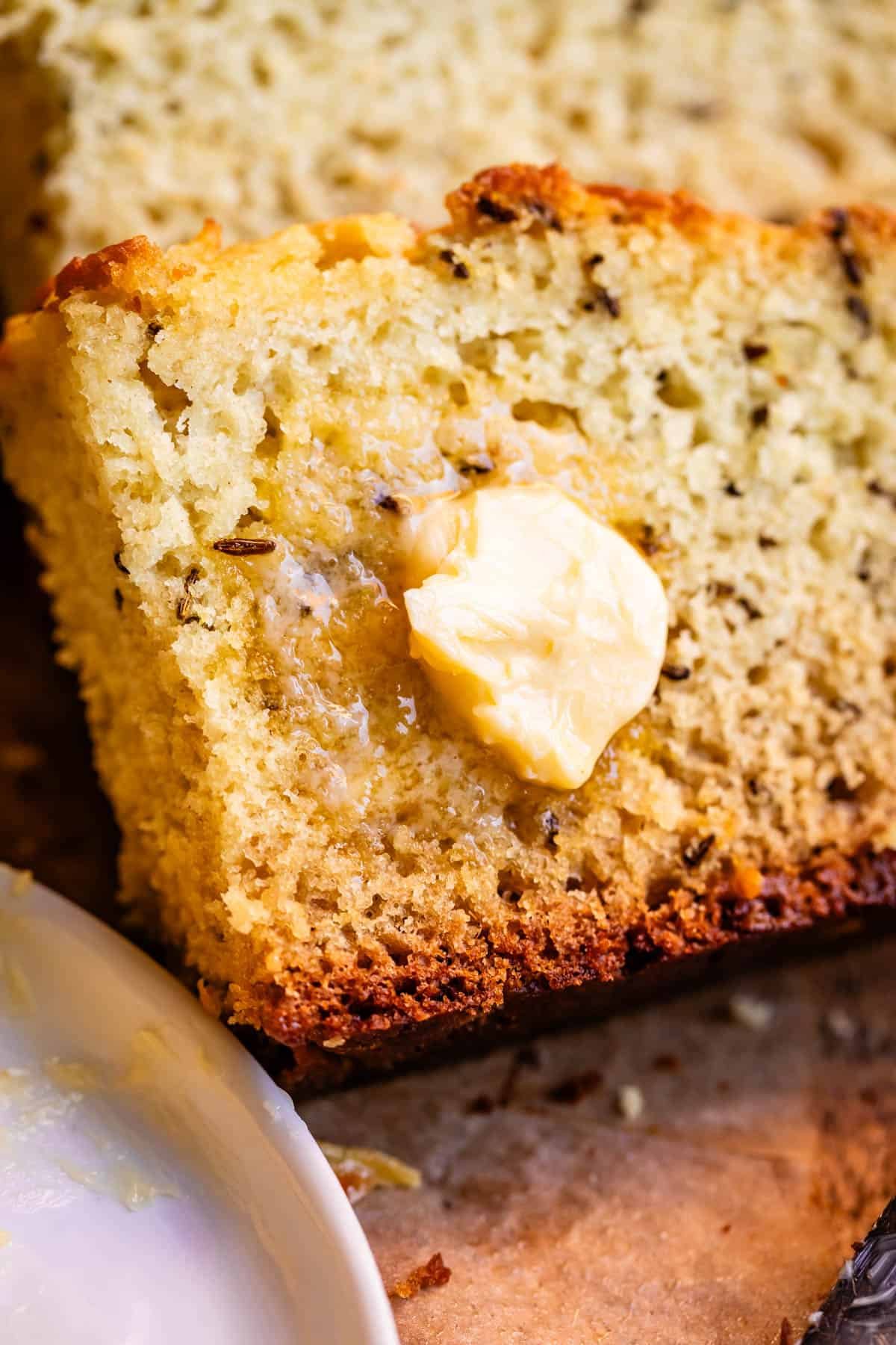 Close up of slice of Irish soda bread showing caraway seed with melting pat of butter.