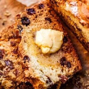 Crusty slice of Irish soda bread by larger loaf and small bowl of blackberry jam.